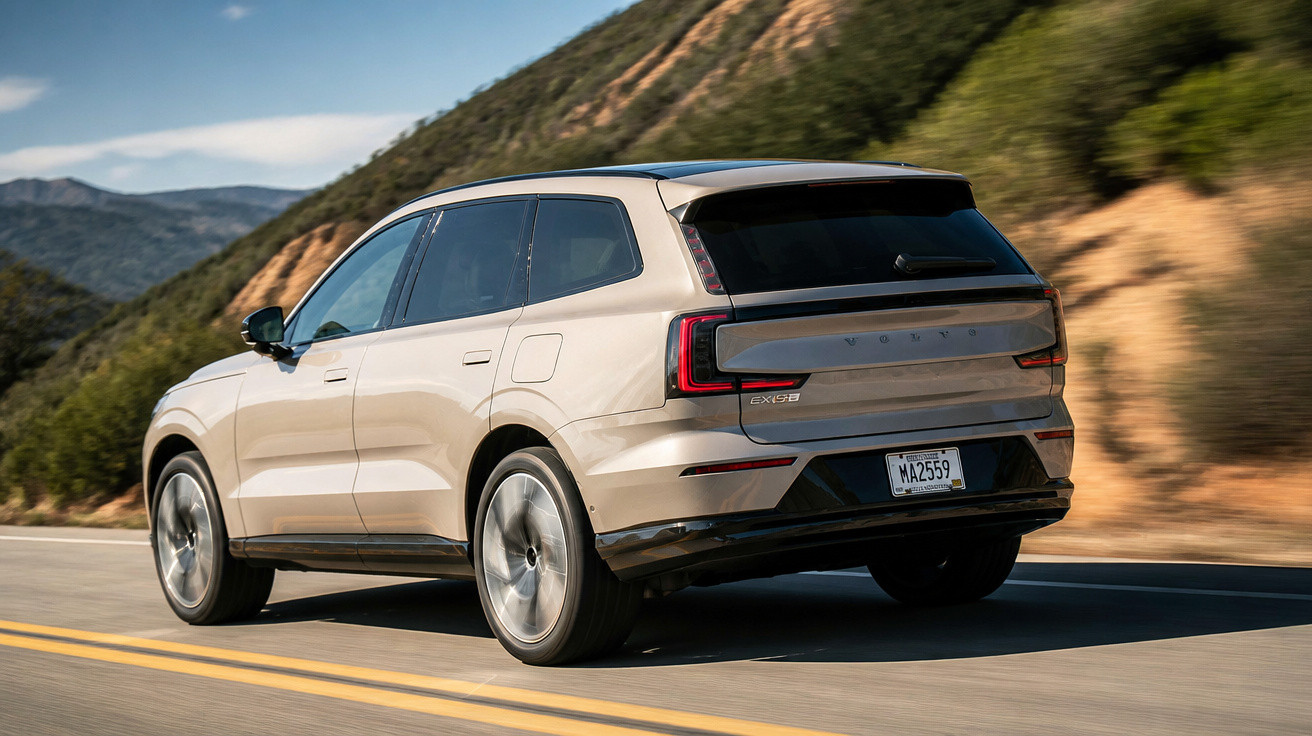 Beige Volvo EX90 electric SUV driving on a mountain road with hills in the background.